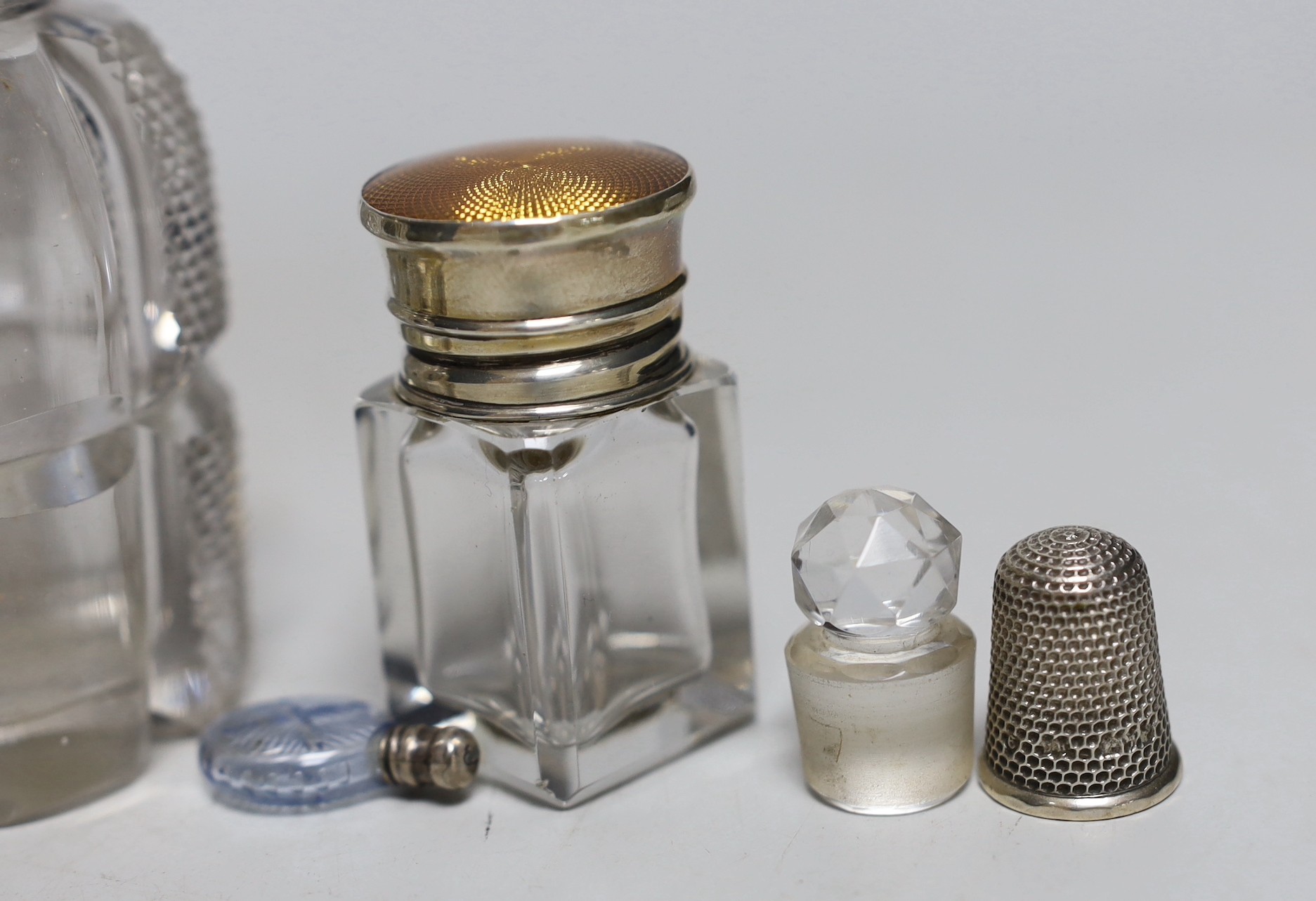 Three silver or white metal mounted glass scent bottles including enamelled, 56mm and ruby glass, one other, two glass stoppers and three thimbles.